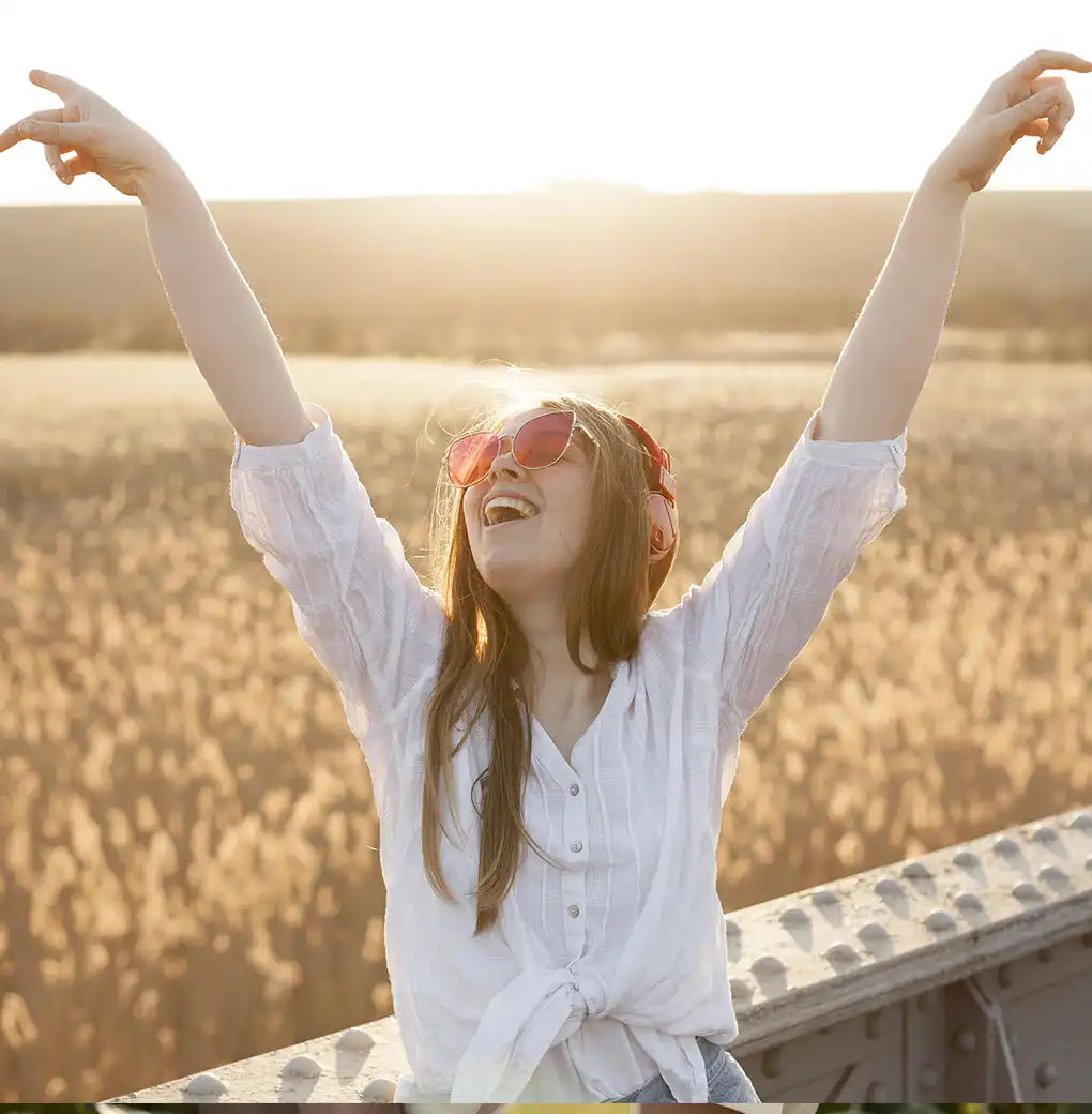 Mujer joven sonriendo con los brazos levantados al sol, disfrutando de un momento de libertad y alegría mientras fortalece su amor propio
