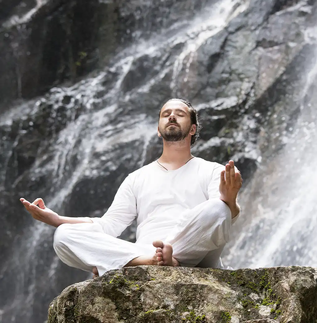 Hombre meditando en posición de loto frente a una cascada, utilizando afirmaciones y decretos para reprogramar su mente y elevar su energía