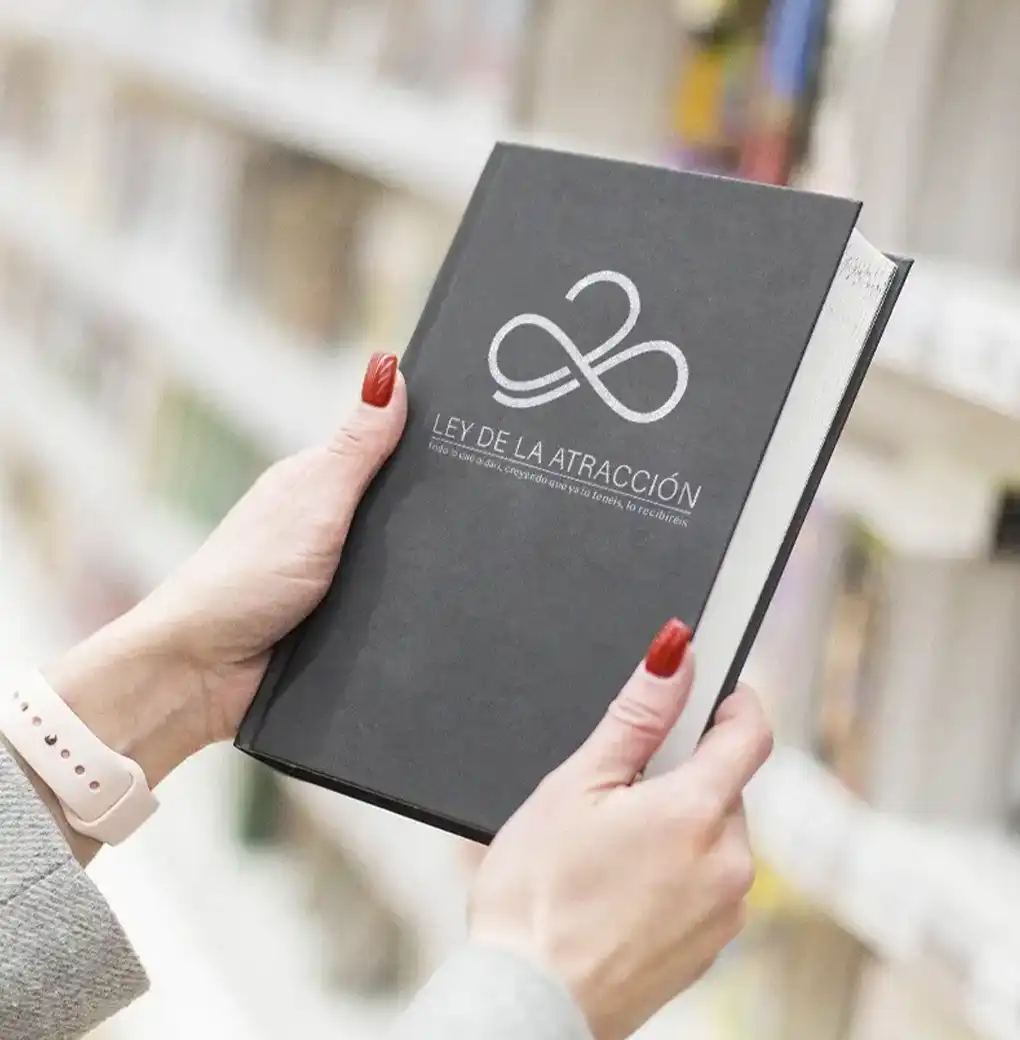 Manos sosteniendo un libro negro sobre la Ley de la Atracción en una librería, simbolizando crecimiento personal y autoayuda