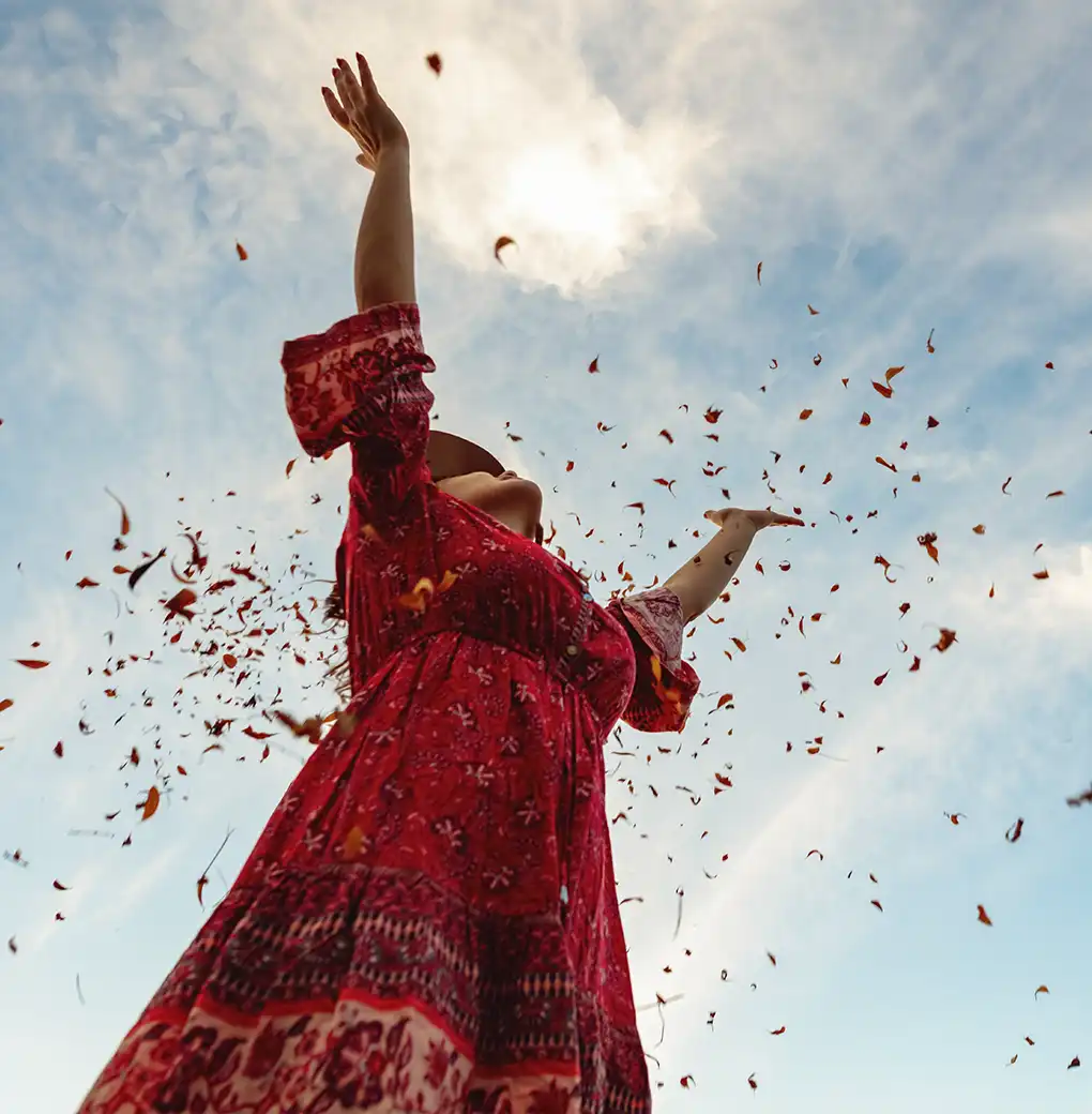Mujer vestida de rojo levantando los brazos al cielo mientras caen pétalos, simbolizando la conexión con la energía de abundancia y prosperidad