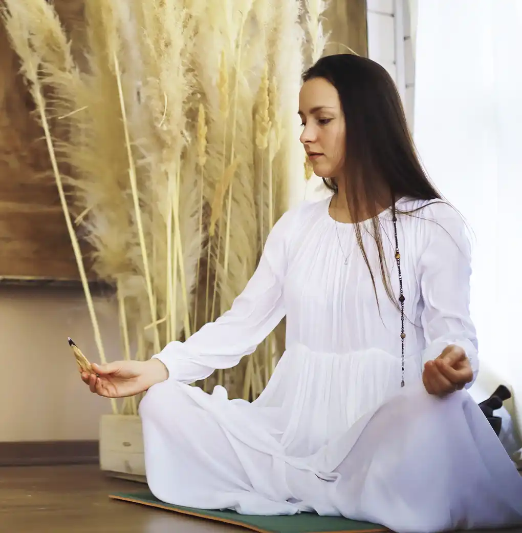 Mujer meditando vestida de blanco en posición de loto, practicando visualizaciones guiadas para entrenar su energía y manifestar nuevas realidades